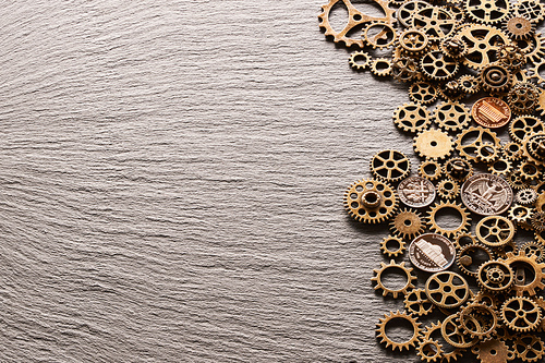 Various metal cogwheels and gear wheels with USA coins over slate background