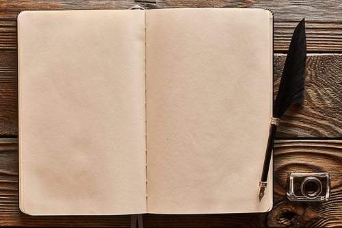 Feather pen and blank notebook page over wooden background