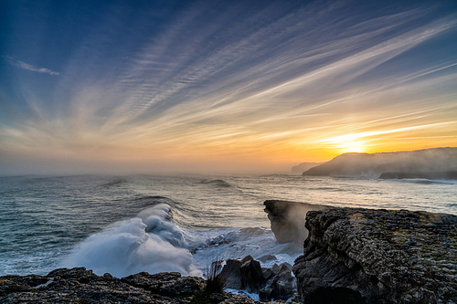 A view of huge storm surge ocean waves crashing onto shore and cliffs at sunrise