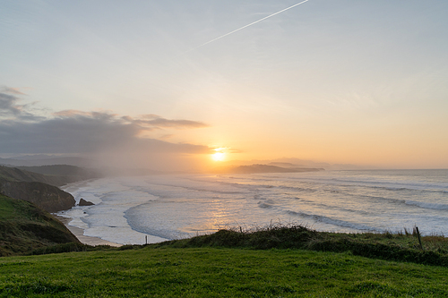 Tall green grassy cliffs drop down to the ocean coast in northern Spain at sunset