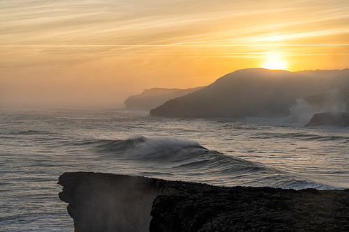 A view of huge storm surge ocean waves crashing onto shore and cliffs at sunrise