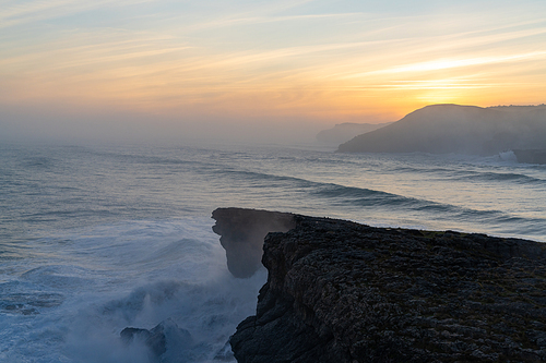 A view of huge storm surge ocean waves crashing onto shore and cliffs at sunrise