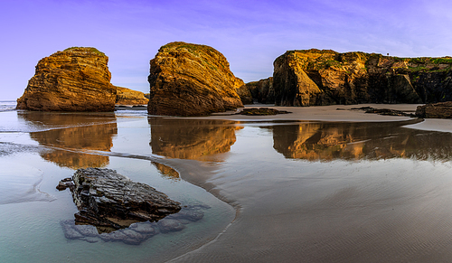 A peaceful sunset on a sandy beach with tidal pools and jagged broken cliffs behind