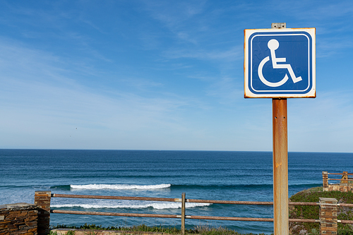 A sign for handicapped parking at a beach access with ocean behind