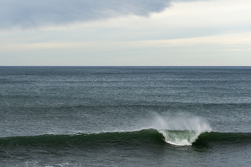 A large wave breaking in the ocean with copy space and blue and cloudy sky