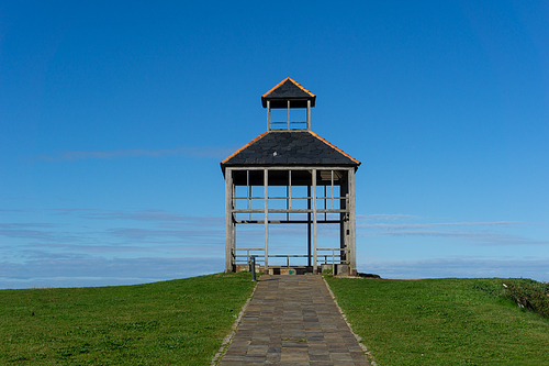 A simple gazebo pavillion with stone walkway in a green meadow under a blue sky