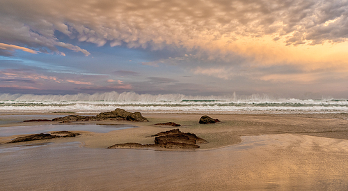 A sunrise on a beautiful empty beach with waves crashing and rocks in the sand