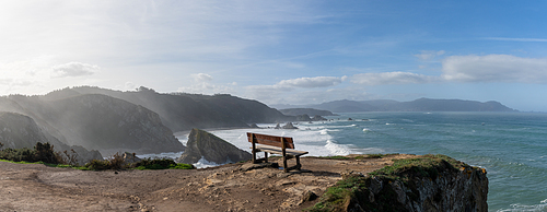 A panorama of scenic viewpoint with wooden bench on beautiful ocean coast with high cliffs and big waves