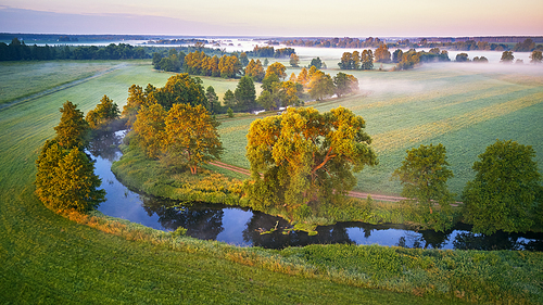 Sunny summer calm morning. Small river, fog sunrise aerial view. First sunrays over green meadow and field