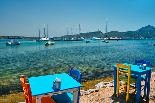 Cafe restaurant table of street cafe with chairs on beach in Adamantas town on Milos island with Aegean sea with boats and yachts in background. Milos island, Greece