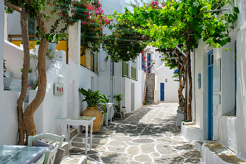 Picturesque narrow street with traditional whitewashed houses with cafe tables of Naousa town in famous tourist attraction Paros island, Greece