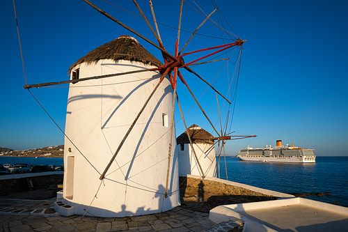 Scenic view of famous Mykonos town windmills. Traditional greek windmills on Mykonos island at sunrise with cruise ship in background, Cyclades, Greece
