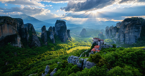 sunset over monastery of Rousanou and Monastery of St. Nicholas Anapavsa in famous greek tourist destination Meteora in Greece on sunset with sun rays and lens flare and dramatic sky