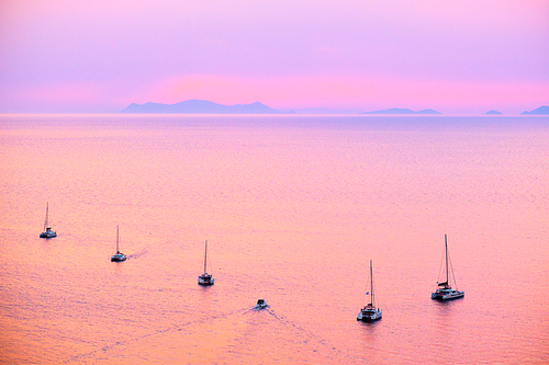 Tourist yachts boat in Aegean sea near Santorini island with tourists watching sunset from viewpoint. Santorini, Greece