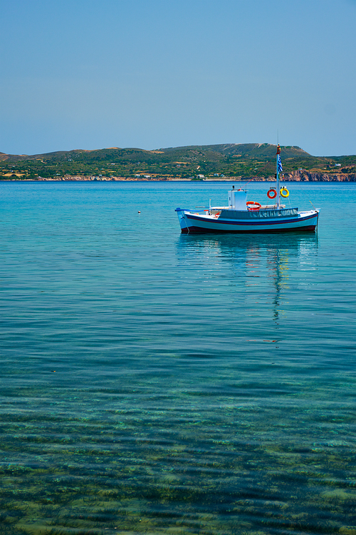 Greek fishing boat moored in blue waters of Aegean sea in harbor of near Milos island, Greece