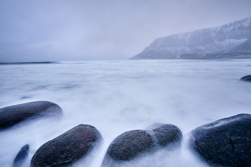 Waves of Norwegian sea surging on stone rocks at Unstad beach, Lofoten islands, Norway in winter storm. Long exposure