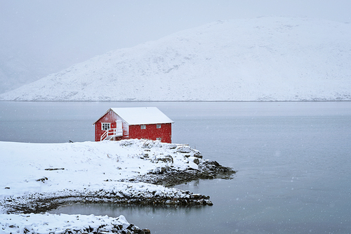 Traditional red rorbu house on fjord shore with heavy snow in winter. Lofoten islands, Norway