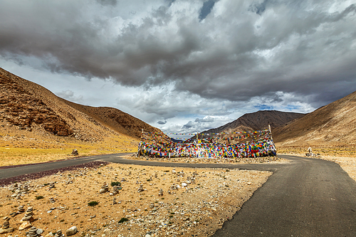 Road and Buddhist prayer flags (lungta) at Namshang La pass in Himalayas. Ladakh, India