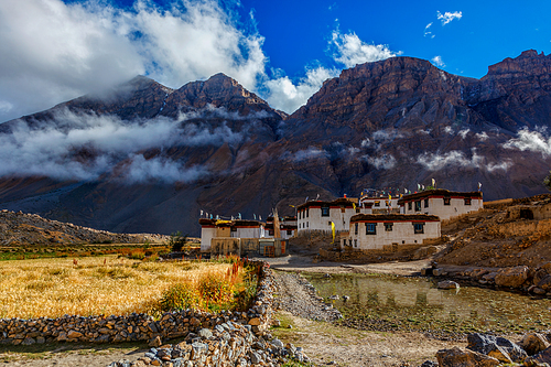 Himalayan landscape with high altitude village in Spiti Valley aslo known as Little Tibet. Whitewashed houses stand just below clouds surrounded by Himalaya chain of mountains. Himachal Pradesh, India