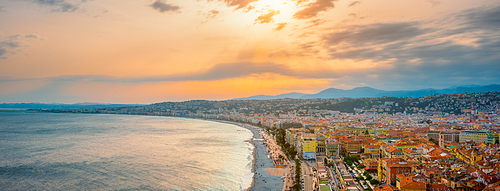 Picturesque scenic panorama of Nice, France on sunset. Mediterranean Sea waves surging on the beach, people are relaxing on the beach, cars driving the road. Nice, France