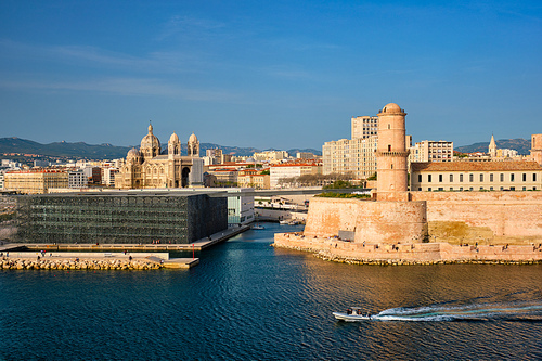 Marseille Old Port and Fort Saint-Jean and Museum of European and Mediterranean Civilisations and Marseille Cathedral on sunset with passing boat. Marseille, France