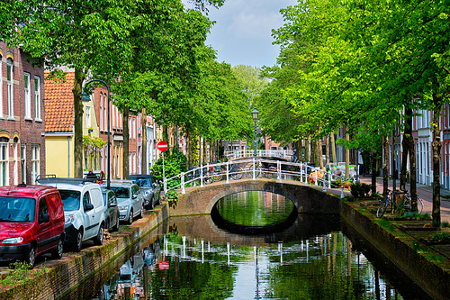 Cars and bicycles parked along the canal in street of Delft with reflection. Delft, Netherlands