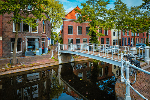 Picturesque Holland cityscape view - bicycle on bridge and canal with cars parked along in street of Delft, Netherlands