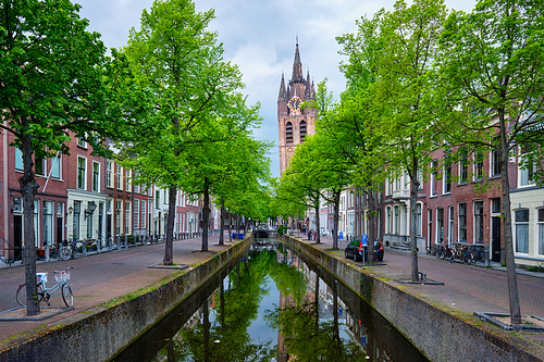 Delt canal with old houses bicycles and cars parked along and Oude Kerk Old church tower. Delft, Netherlands