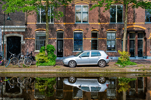 Cars and bicycles parked along the canal in street of Delft with reflection. Delft, Netherlands