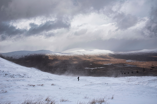 Beautiful Winter landscape image from mountain top in Scottish Highlands down towards Rannoch Moor during snow storm and spindrift off mountain top in high winds