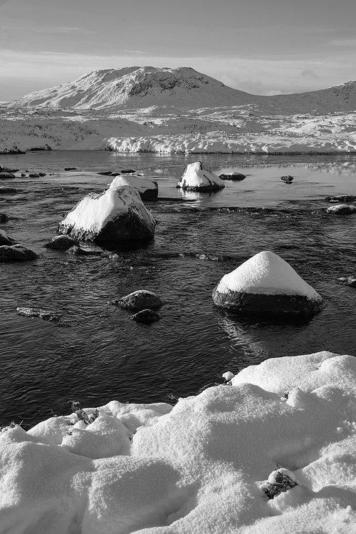 Black and white Majestic Winter landscape image looking towards Scottish Highlands mountain range across Loch Ba on Rannoch Moor