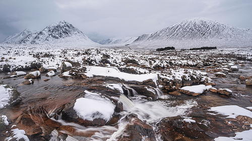 Beautiful Winter landscape image of River Etive in foreground with iconic snowcapped Stob Dearg Buachaille Etive Mor mountain in the background