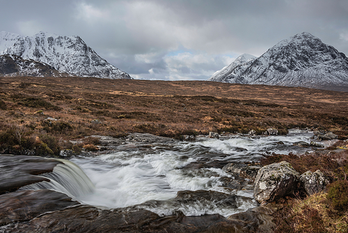 Beautiful Winter landscape image of River Etive in foreground with iconic snowcapped Stob Dearg Buachaille Etive Mor mountain in the background