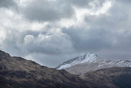 Lovely landscape image of snowcapped Ben Lomond mountain peak in Scottish Highlands with dramatic sky above