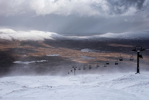 Beautiful Winter landscape image from mountain top in Scottish Highlands down towards Rannoch Moor during snow storm and spindrift off mountain top in high winds