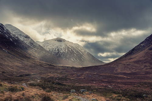 Epic Winter landscape image of Etive Mor in Scottish Highlands with sunbeams streaming down between the mountain peaks