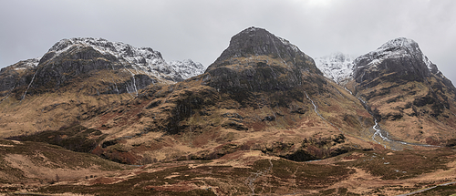 Epic Winter landscape image of snowcapped Three Sisters mountain range in Glencoe Scottish Highands with dramatic sky