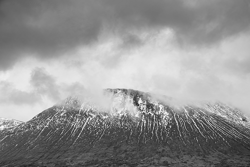 Black and white Beautiful Winter landscape image of Beinn A’ Chaladair in Scotland with dramatic skies overhead