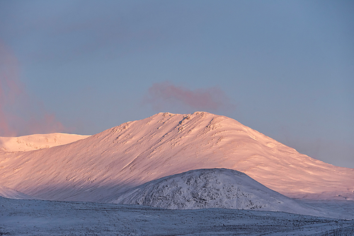 Beautiful Alpen Glow hitting mountain peaks in Scottish Highlands during stunning Winter landscape sunrise