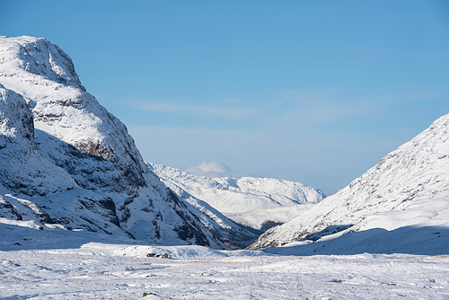 Beautiful Winter landscape blue sky image of view along Glencoe Rannoch Moor valley with snow covered mountains all around