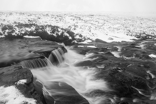 Black and white Beautiful Winter landscape image of River Etive in foreground with iconic snowcapped Stob Dearg Buachaille Etive Mor mountain in the background