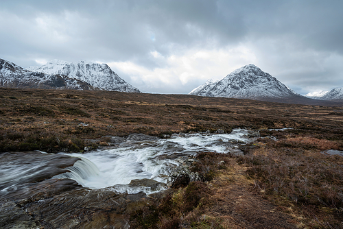 Beautiful Winter landscape image of River Etive in foreground with iconic snowcapped Stob Dearg Buachaille Etive Mor mountain in the background