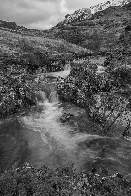 Black and white epic landscape image of River Coe in Scottish Highlands with mountains in background