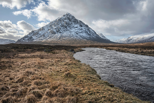 Beautiful Winter landscape image of River Etive in foreground with iconic snowcapped Stob Dearg Buachaille Etive Mor mountain in the background