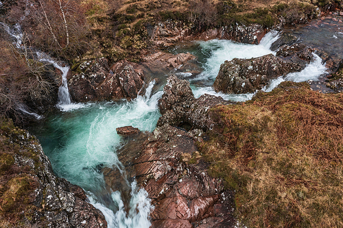 Beautiful aerial drone landscape image of vibrant River Coe flowing beneath snowcapped mountains in Scottish Highlands