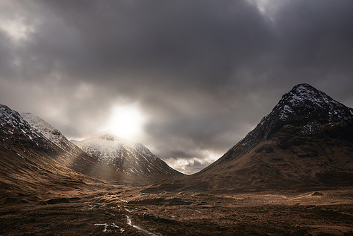 Epic Winter landscape image of Etive Mor in Scottish Highlands with sunbeams streaming down between the mountain peaks