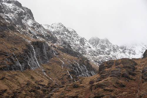 Epic Winter landscape image of snowcapped Three Sisters mountain range in Glencoe Scottish Highands with dramatic sky