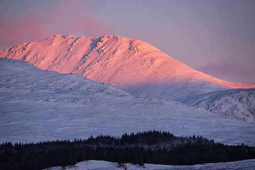 Beautiful Alpen Glow hitting mountain peaks in Scottish Highlands during stunning Winter landscape sunrise