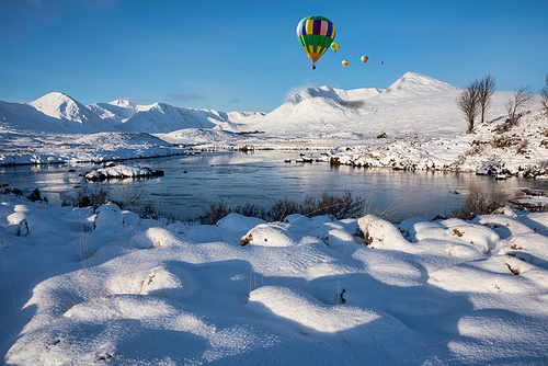 Digital composite image of hot air balloons flying over Majestic Winter landscape image looking towards Scottish Highlands mountain range across Loch Ba on Rannoch Moor