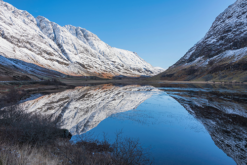 Beautiful Winter landscape image of Loch Achtriochan in Scottish Highlands with stunning reflections in still water with crytal clear blue sky